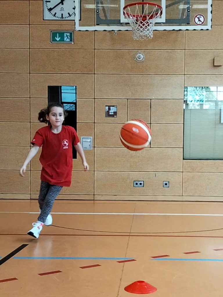 Ein Mädchen holt nach einem Korbwurf ihren Basketball wieder