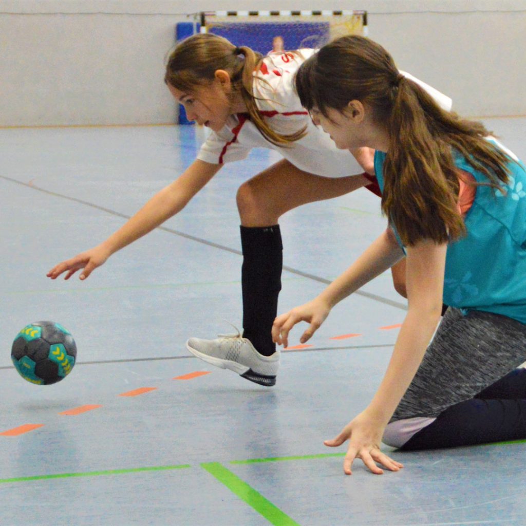 Zwei Mädchen greifen am Boden nach dem Handball