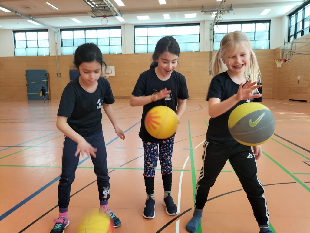 Drei Mädchen stehen nebeneinander und versuchen verschiedene Basketball-Dribbel-Tricks