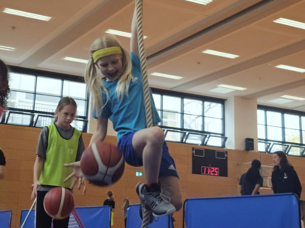 Ein Mädchen schwingt an einem herabhängenden Tau und versucht dabei ihren Basketball zu halten